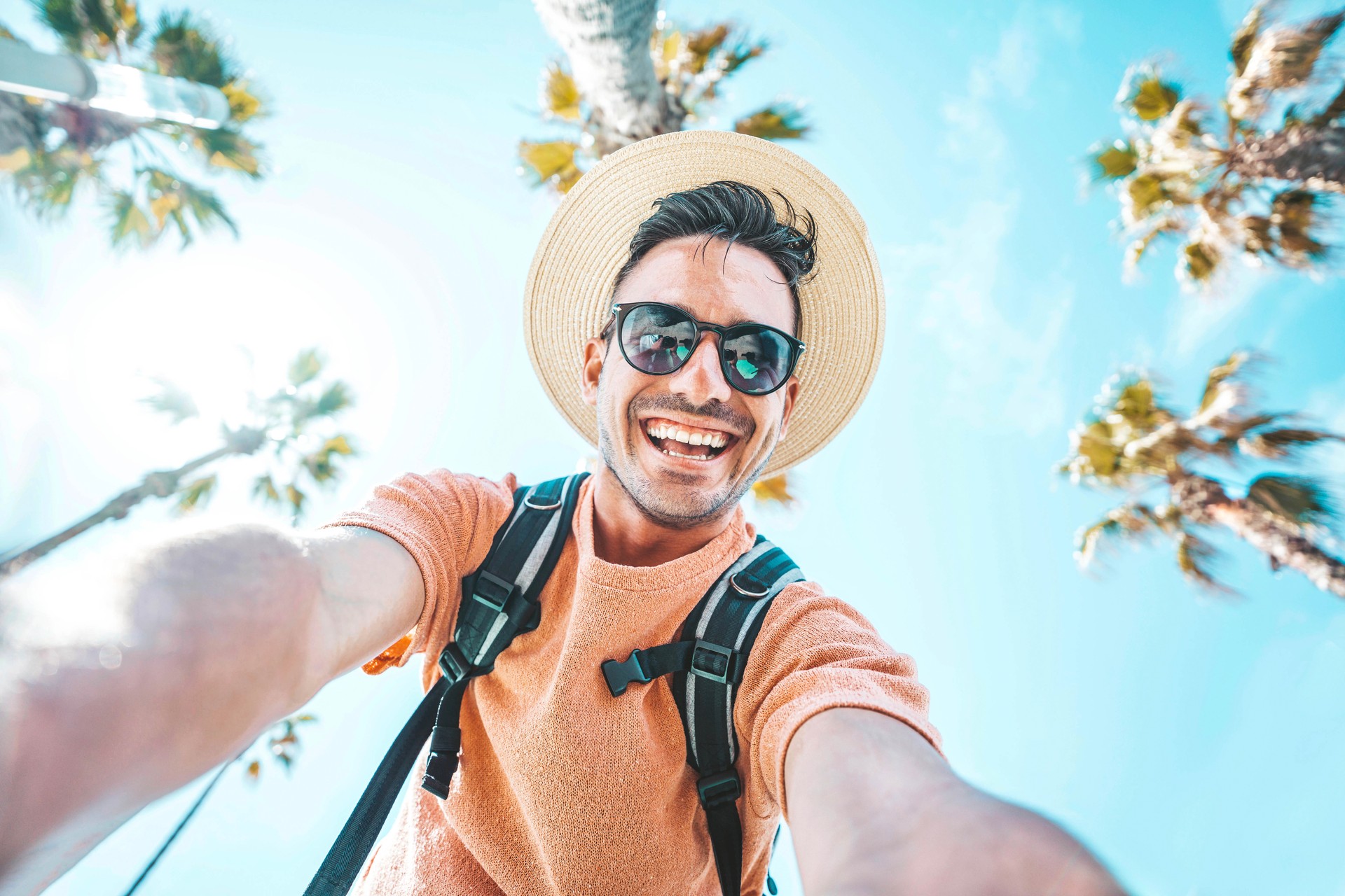 Happy tourist taking self portrait outside with cellphone on summer vacation - Handsome young man laughing at camera enjoying summertime day out - Tourism, traveler life style and technology concept